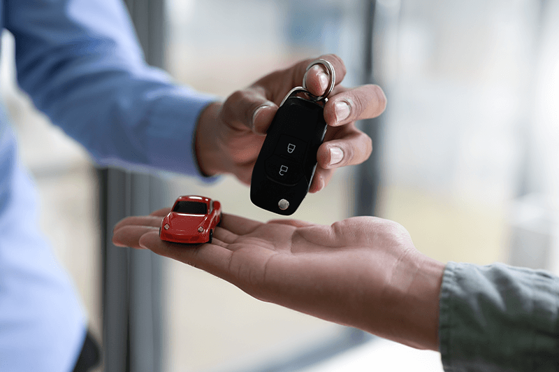 Persona haciendo entrega de un coche pequeño a cambio de llaves del coche, representando la normativa para comprar el coche